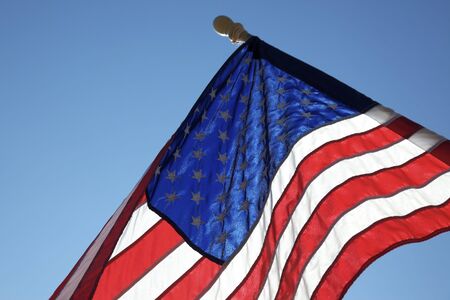 The American flag hangs proudly with a blue sky background on Main Street in Hometown America.の写真素材