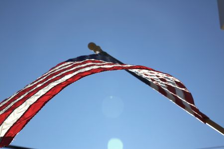 The American flag hangs proudly with a blue sky background on Main Street in Hometown America.の写真素材
