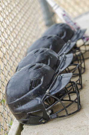Softball helmets, in the dugout getting ready to play a game on a sunny day, with a bat in the...