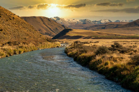 Ashburton Lakes District stream heading through the valley to the snow capped Southern Alpsの写真素材