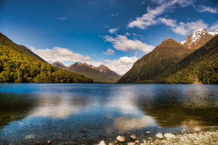 Snow capped southern alps reflected on the water of a beautiful lake in Fiordland New Zealandの写真素材