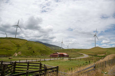 Rural agricultural scenery of a farm and its sheep and cattle yards on the  hills and valleys with electricity generating wind turbines on the peaksの写真素材