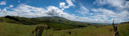 Panoramic view of rural farm grazing countryside of hills and valleys with wind turbines on the peaksの写真素材