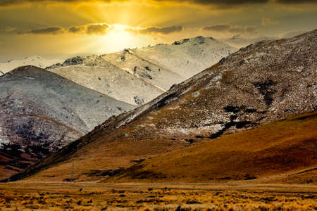 Mystical magical golden light and sun rays shing down on the arid dry tundra of rge valleys and lower slopes of the Southern Alpsの写真素材