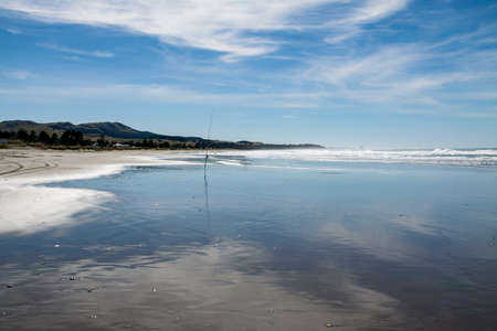 Lone surf casting fishing rod stuck in the sand at the desolated empty coastal beachの写真素材