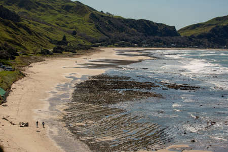 Two unknown surfers walking along the beach at low tide with the rocks exposedの写真素材