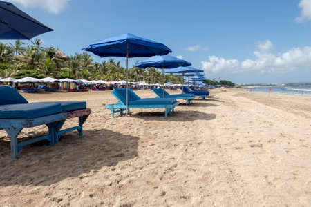 A row of empty sun loungers and umbrellas waiting for tourists on Kuta beach Bali Indonesiaの写真素材