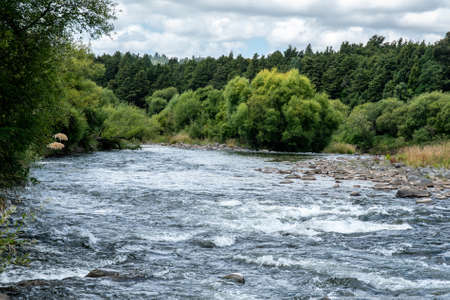 swift moving river lined by trees running through rural countryside