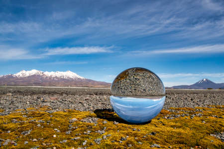 The Central Plateau snow capped volcanoes in the Desert road reflected in a crystal ball sitting on some yellow moss at the side of State Highway oneの写真素材