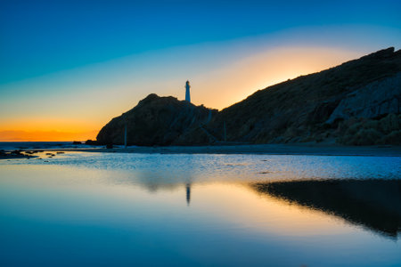 CastlePoint lighthouse and the early signs of sunlight reflected in the calm waters of the lagoon as the sun rises at dawnの写真素材
