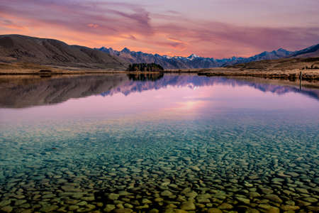 Transparant crystal clear water showing the rocks on the bottom of the lake with mountain reflections at sunsetの写真素材
