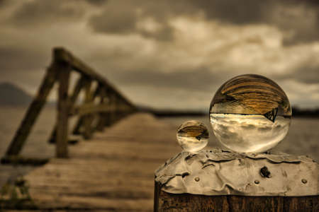Arty abstract view of the Old wooden Tokaanu wharf, lake Taupo in moody cloudy rainy weather featuring two crystal ballsの写真素材