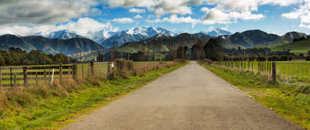 Rural country road heading through agricultural farming land  to the snow covered Tararua Rangesの写真素材