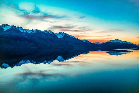 Magical vibrant sunset and red skies over Lake Wakatipu with the mountain range reflected on the calm waterの写真素材