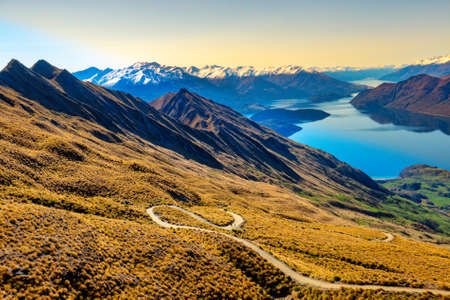 Hikers tramping  the winding path to the top of Roys Peak overlooking the lake and snow capped Southern Alps near Wanakaの写真素材