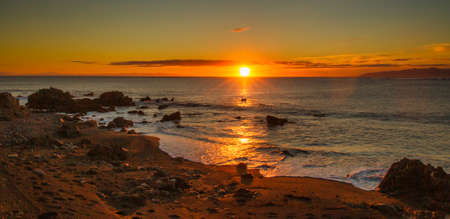 The rugged wild coastline at Cape Palliser with a magnificent vibrant sunset on the horizonの写真素材