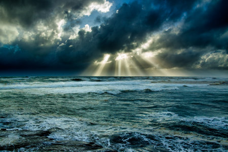 Beams of light in the midst of a dark storm over the coast at Muriwai beachの写真素材