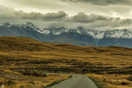 Driving towards the snow covered Southern alps on a windy gravel road through rural farmland  between Lake Takapo and Lake Pukakiの写真素材
