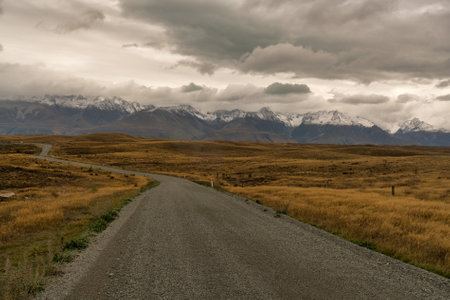 Driving towards the snow covered Southern alps on a windy gravel road through rural farmland  between Lake Takapo and Lake Pukakiの写真素材
