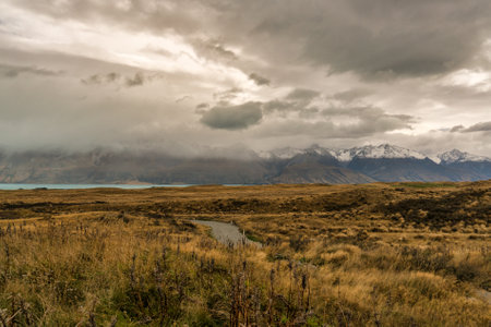 Driving towards the snow covered Southern alps on a windy gravel road through rural farmland  between Lake Takapo and Lake Pukakiの写真素材