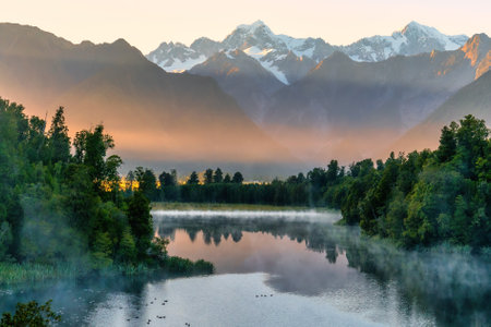 First early morning light of the day at the beautiful Lake Matheson  on the West Coast with some mist rising around the lakeshoreの写真素材