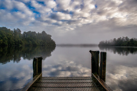 Early morning fog with low cloud at sunrise above the surface of the West Coast lakeの写真素材