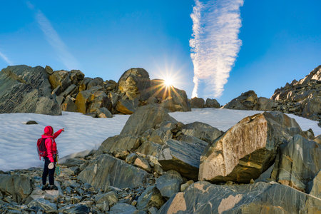 A woman in a red jacket stands on the edge of a mountain and looks at the sunrise.の写真素材