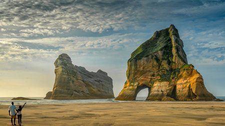 Two tourists enjoying the seaside scenery at the Archway islands on Wharariki beachの写真素材