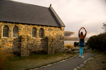 A young woman standing in front of an old church and making a heart with her handsの写真素材