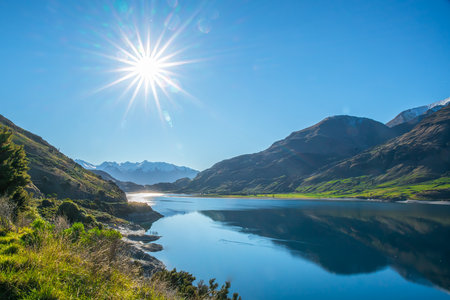 Coastline at Lake Wanaka on a beautiful sunny day with a sun flare in the cloudless sky
