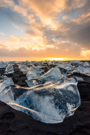 Sunset light reflected on a block of ice in the volcanic black sand of the Diamond Beach, Icelandの写真素材