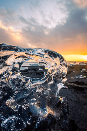 Sunset light reflected on a block of ice in the volcanic black sand of the Diamond Beach, Icelandの写真素材