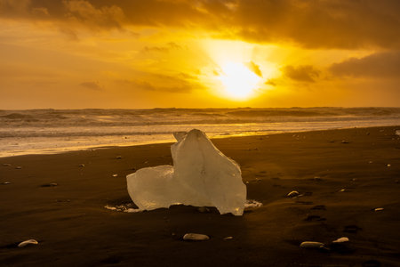 Sunset light reflected on a block of ice in the volcanic black sand of the Diamond Beach, Iceland