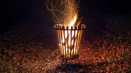 Night shot of a burning fire in a metal basket with leaves on the groundの写真素材