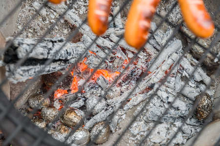 Cooking grate with sausages at a old fire pot with baked potatoの写真素材
