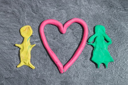 Man and woman with heart made of play dough in front of gray backgroundの写真素材