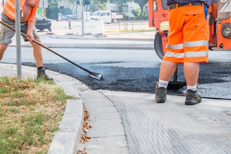 Road workers distributing the hot asphalt with shovels on the road, Germany