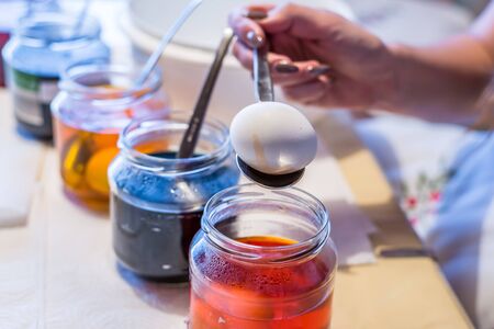 Young woman dyeing Easter eggs at home in the kitchen at the cucumber glass and with different colors, Germanyの写真素材