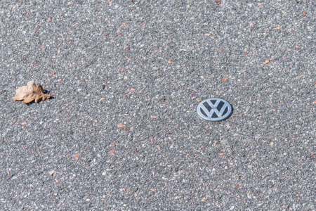 Grafenau, Bayern, Germany, March 15, 2020, VW logo lies on the asphalt of a road with a wilted leafのeditorial素材