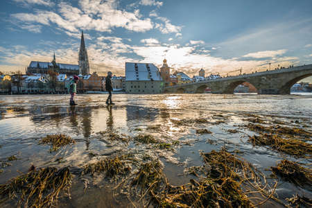 Sunset during flood of Danube river in winter 2021 in Regensburg with view of cathedral the old town and flooded promenade and the stone bridge, Germanyの写真素材