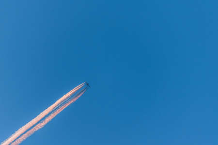Airplane in a blue cloudless sky with colored colorful contrails without clouds during sunset and golden hour, Germanyの写真素材