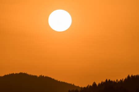 Close up of sun during sunset over horizon with mountain hill landscape in foreground, Germanyの写真素材