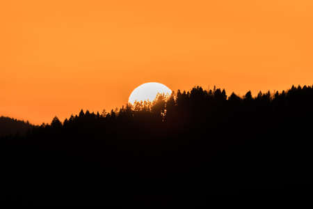 Close up of sun during sunset over horizon with mountain hill landscape in foreground, Germanyの写真素材