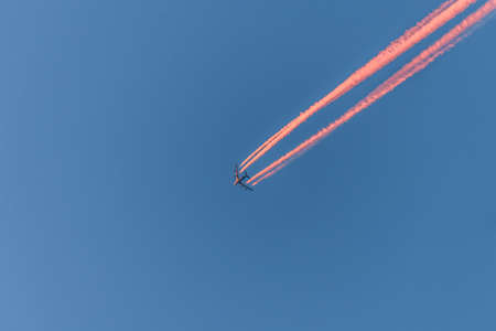 Airplane in a blue cloudless sky with colored colorful contrails without clouds during sunset and golden hour, Germanyの写真素材