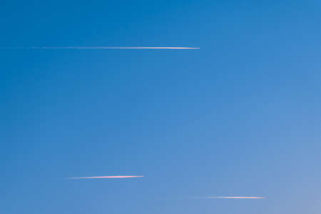 Airplane in a blue cloudless sky with colored colorful contrails without clouds during sunset and...
