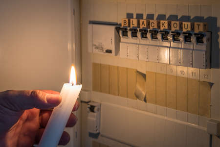 Fuse box with fuses in a distribution box during a power outage lit with white candle holding a man with the word blackout as text, Germanyの写真素材
