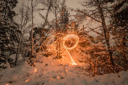 Golden sparks spray at night in the snow on mountain the sparks by glowing steel wool thrown in a circle, Germanyの写真素材