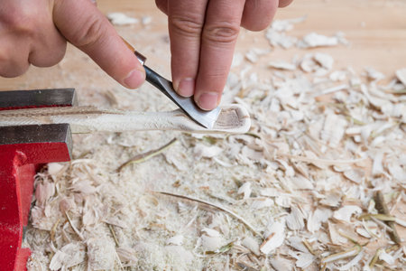 Self carved wooden spoon clamped in vice worked with knife tool on a workbench with wood chips, Germanyの写真素材