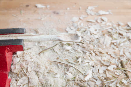 Self carved wooden spoon clamped in vice worked with knife tool on a workbench with wood chips, Germanyの写真素材