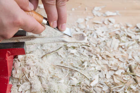 Self carved wooden spoon clamped in vice worked with knife tool on a workbench with wood chips, Germanyの写真素材